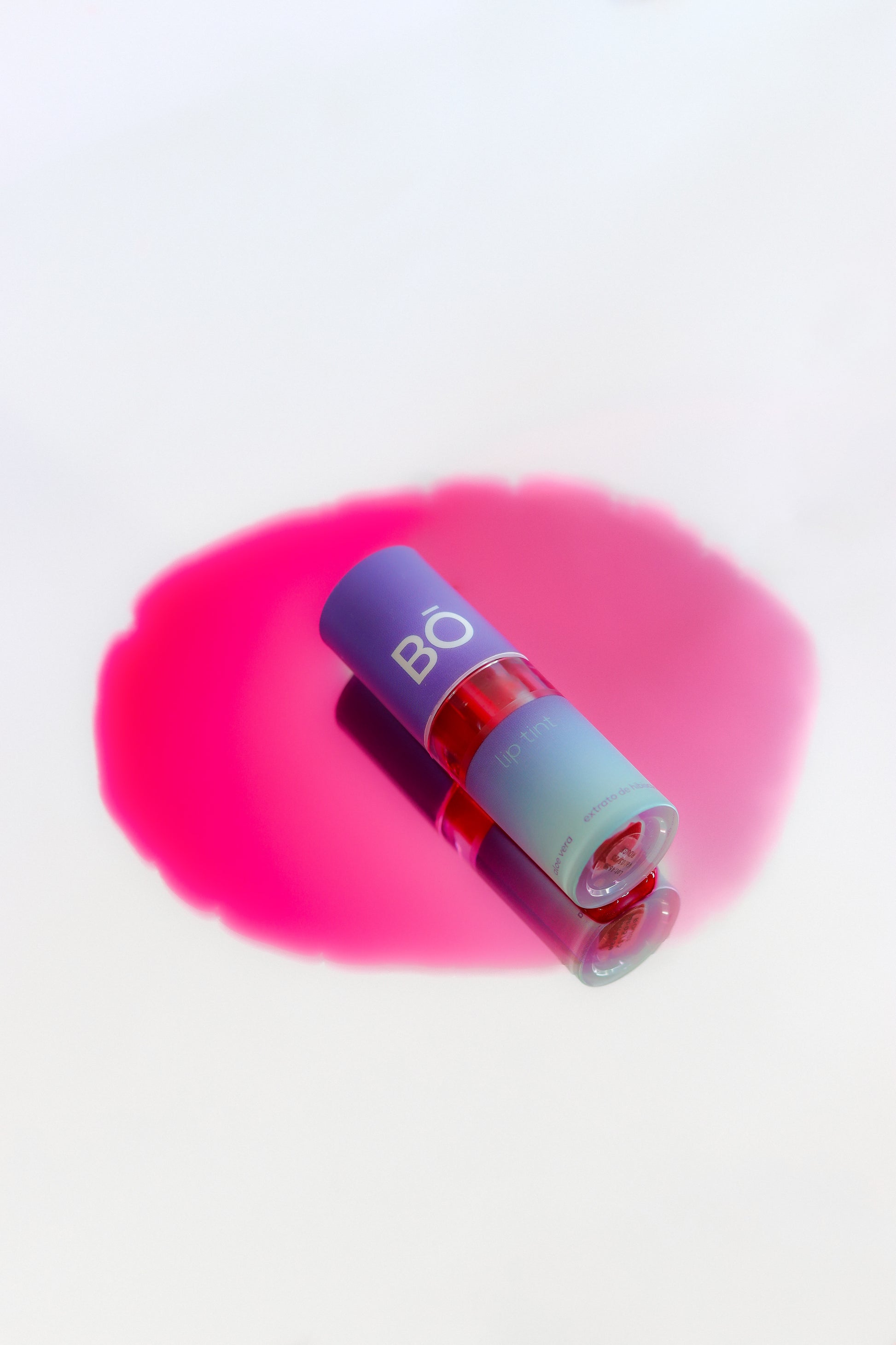 Embalagem de batom líquido lip tint na cor rosa forte derramado sobre fundo espelhado